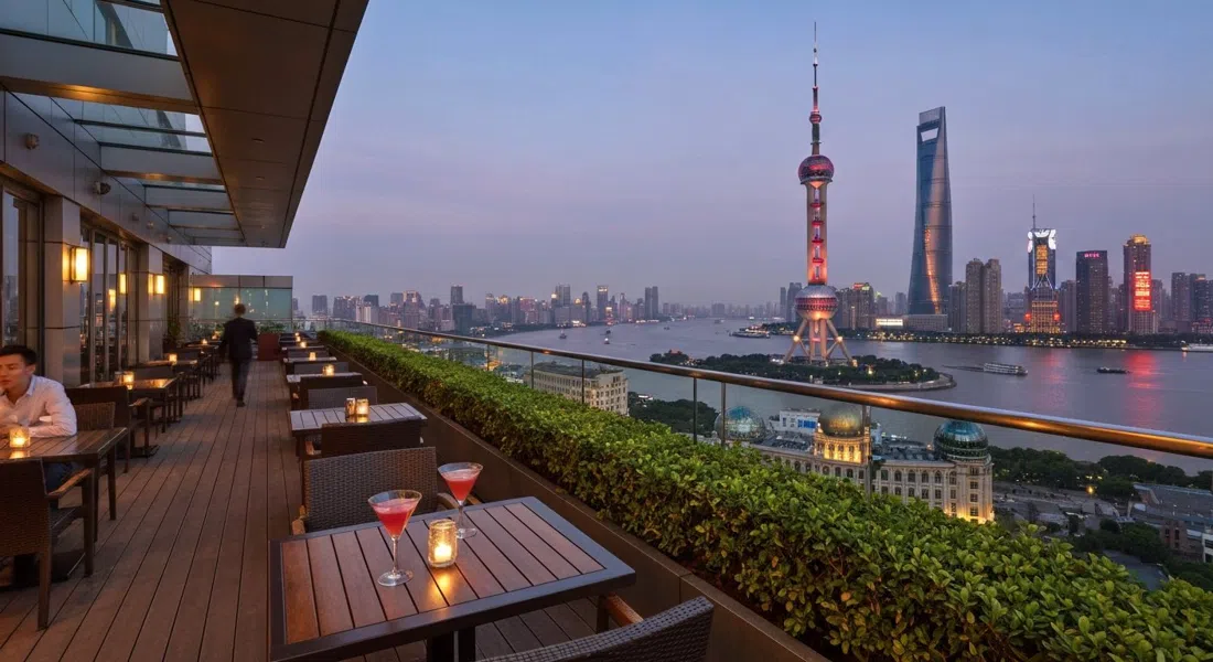 la terraza al aire libre de Flair en el piso 58 del Ritz-Carlton Pudong al atardecer, cócteles sobre las mesas y la Torre Perla Oriental brillando al otro lado del río